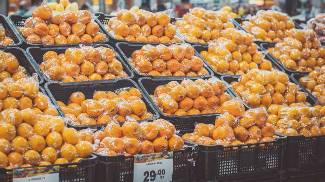 Stack of fresh oranges wrapped in plastic at a grocery store, priced with tags.