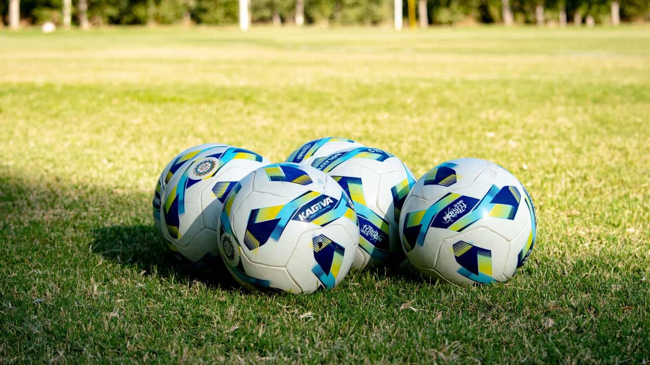Five soccer balls rest on a green field, ready for a game in Mendoza, Argentina.