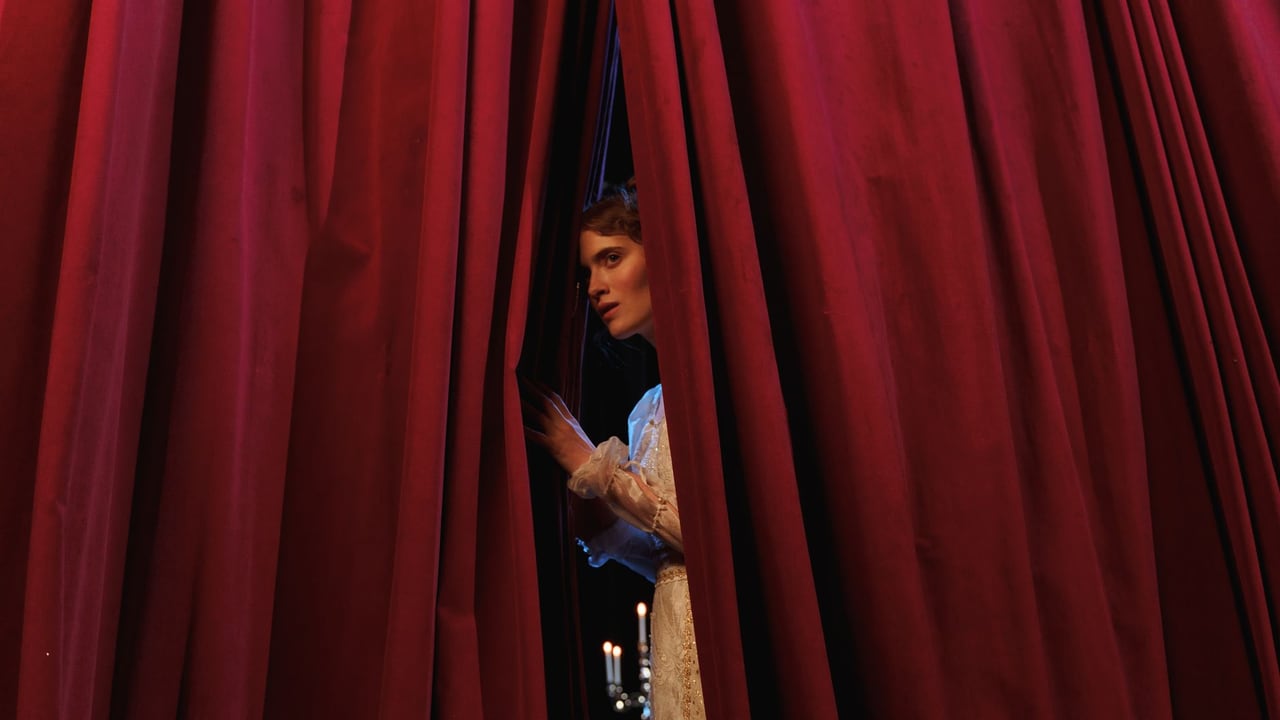 Woman peeks through red theater curtains, capturing a theatrical moment.