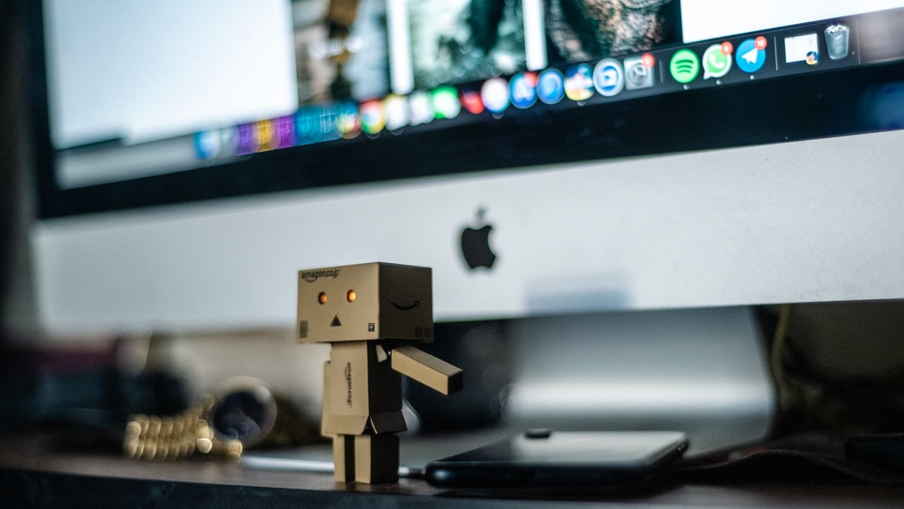 A small cardboard robot toy displayed in front of a computer screen, adding charm to the workspace.
