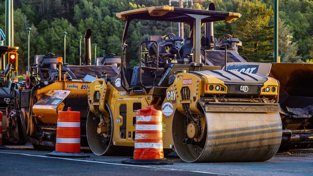 Construction machinery and vehicles on site with road rollers and cones.