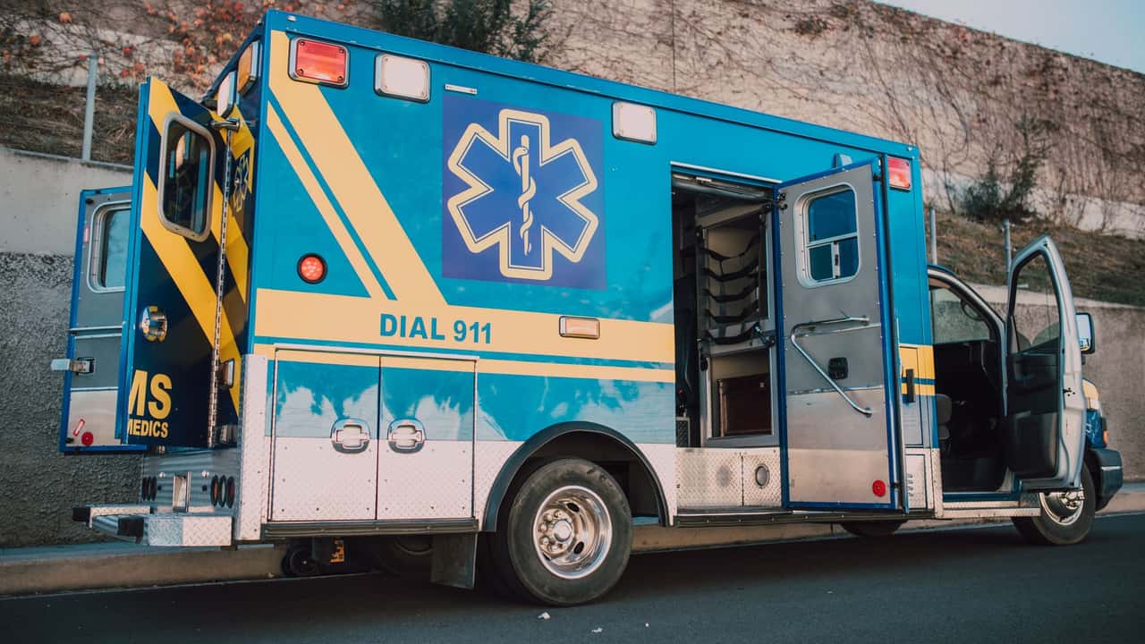 Blue ambulance parked on roadside with open doors, emergency medical service vehicle.