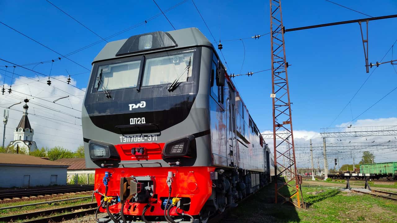 A modern freight train parked on railway tracks under a clear blue sky.