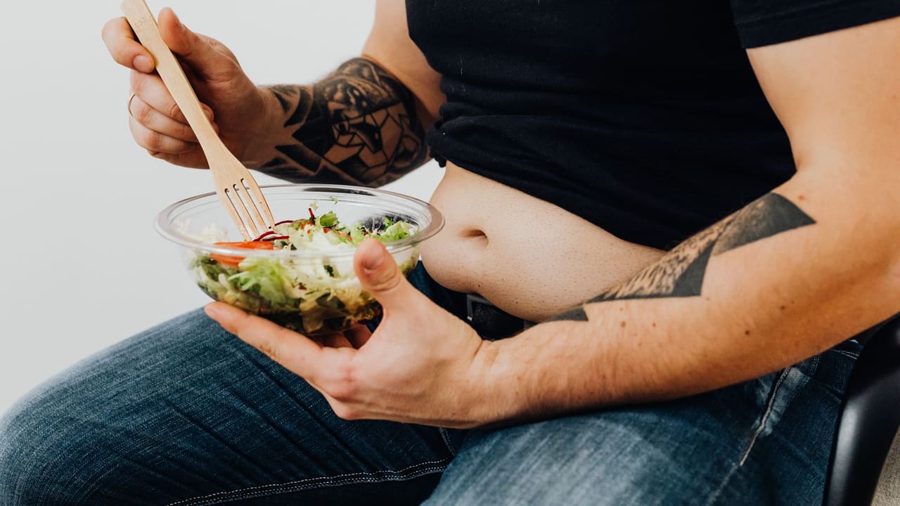 A tattooed individual holding a fresh salad, symbolizing healthy lifestyle and fitness motivation.