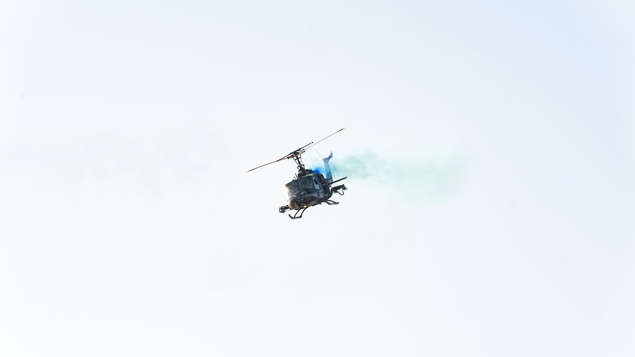 High-altitude helicopter emitting blue smoke in clear El Salvador sky.