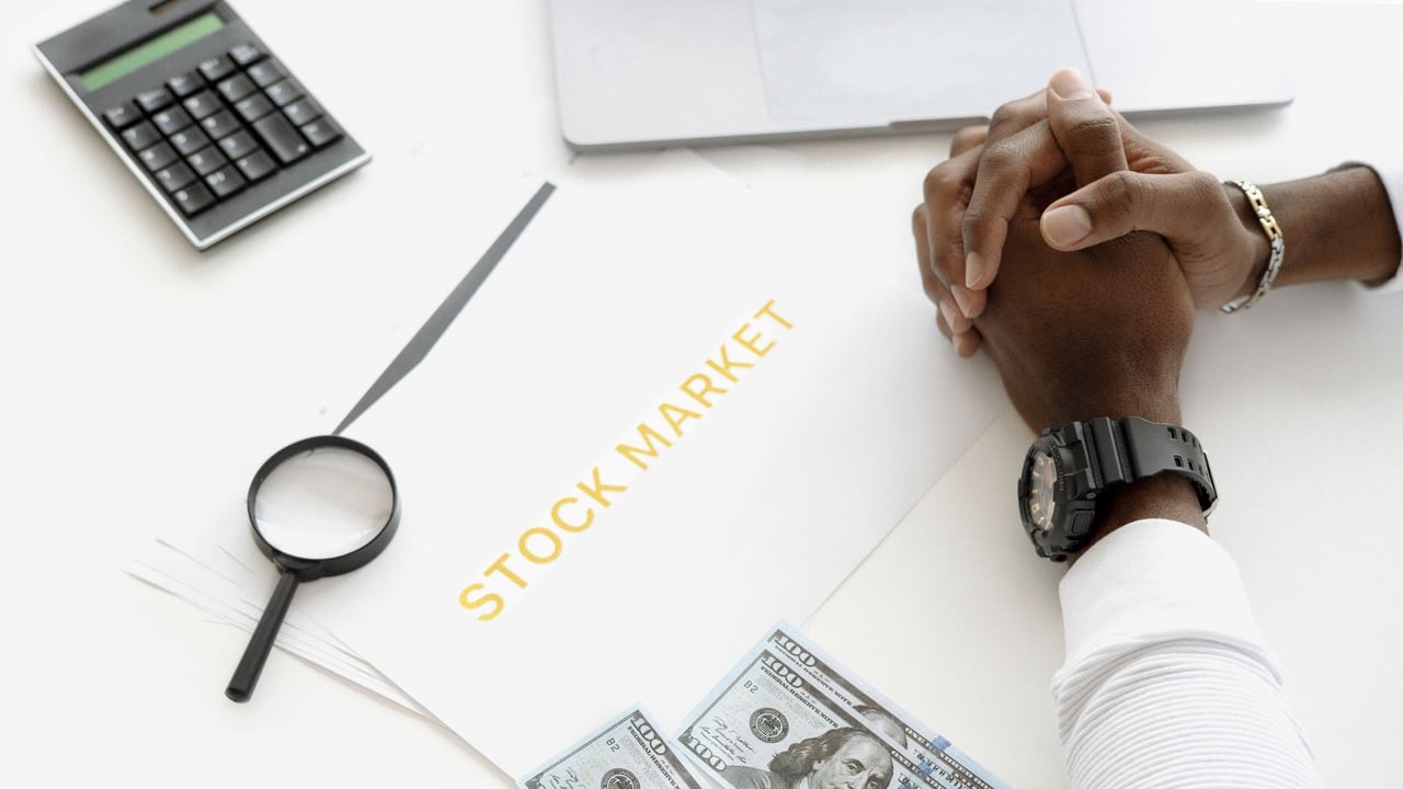 Hands folded over stock market documents with calculator and cash on desk.