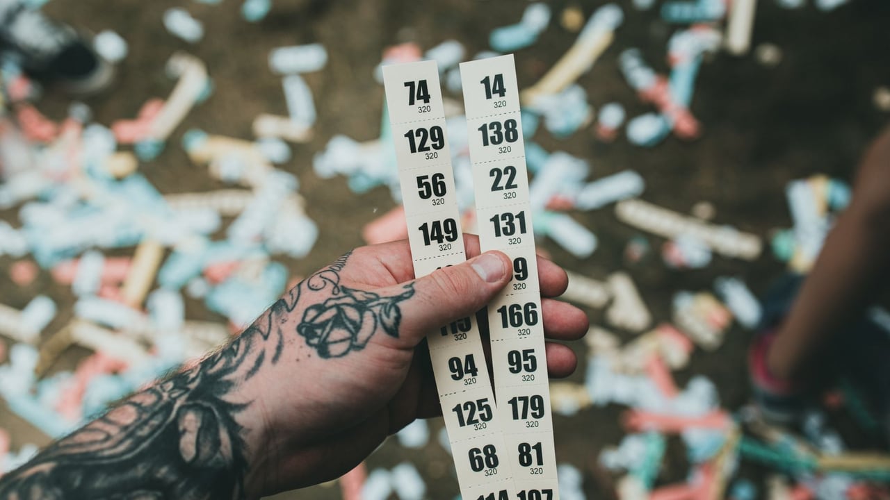 Close-up of a tattooed hand holding raffle tickets amidst confetti at a festival setting.