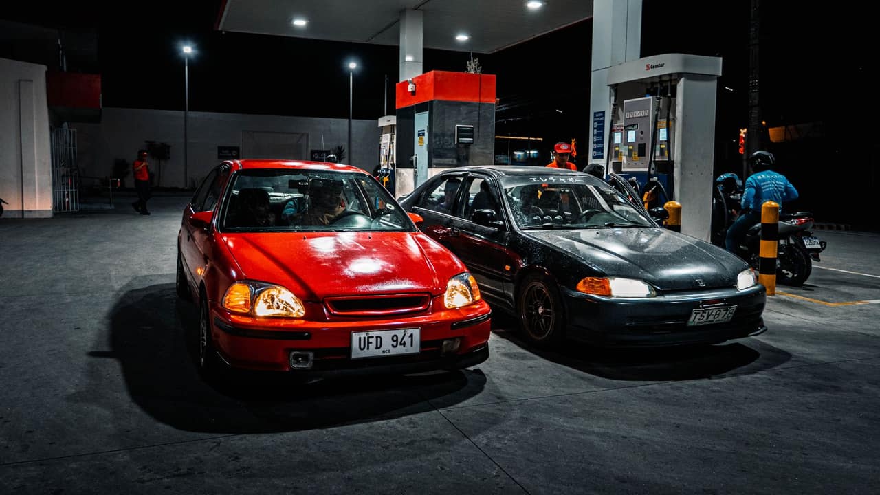 Two cars parked at a gas station at night, illuminated by overhead lights.