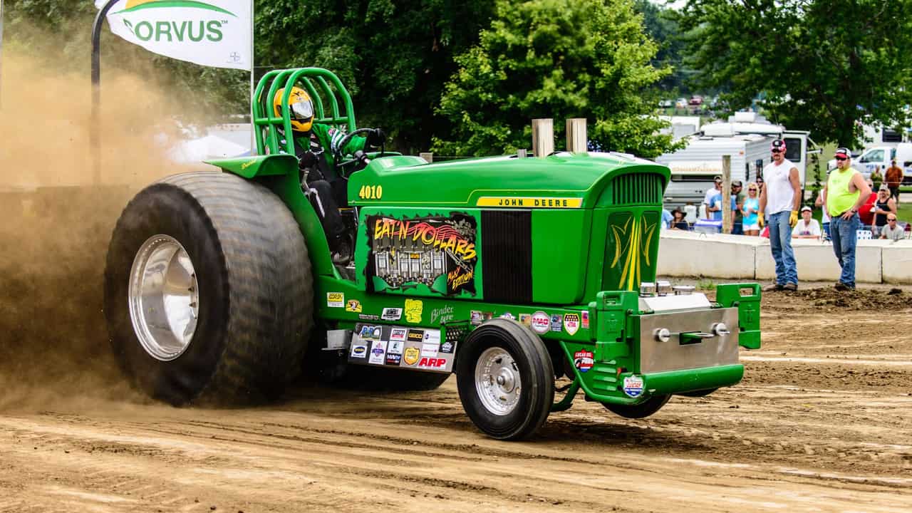 Green tractor in a high-energy pull competition at an outdoor event.