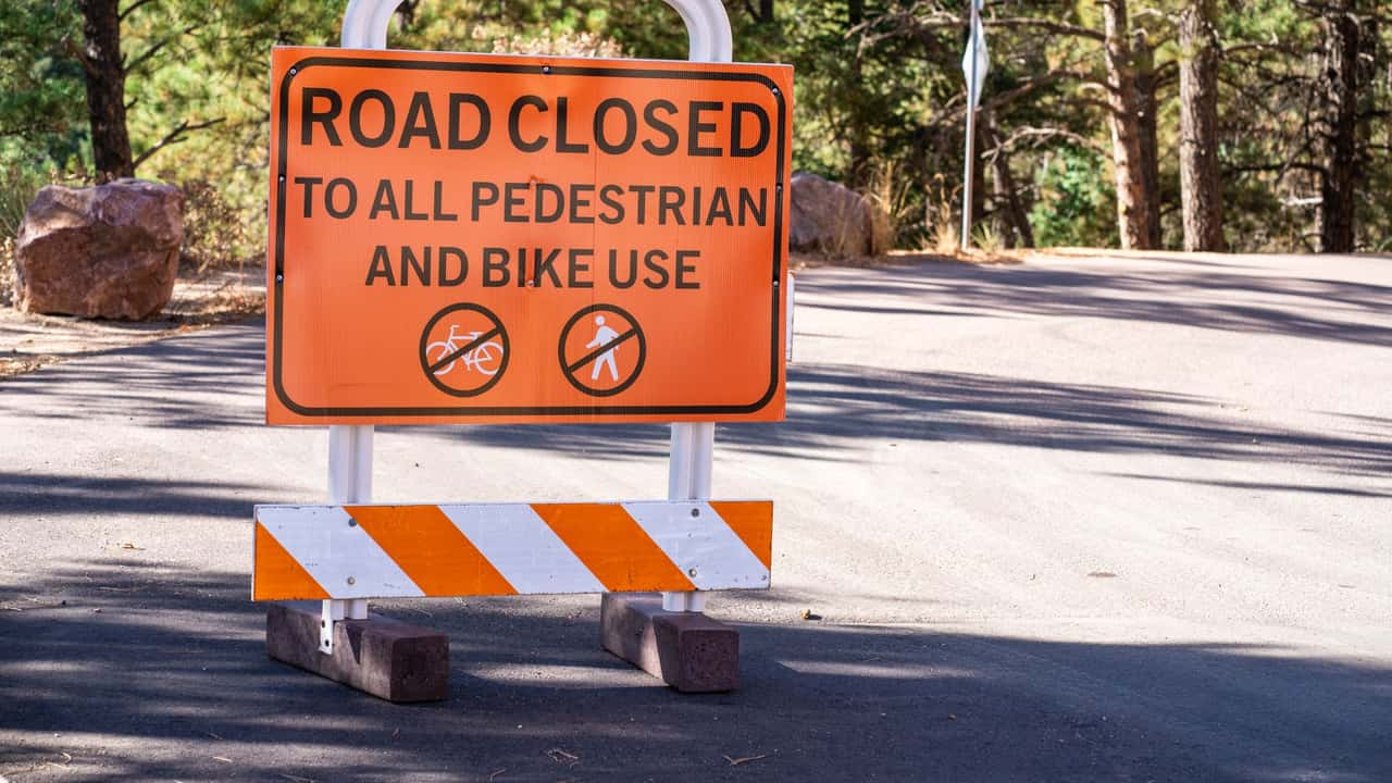Bright road closed sign restricting pedestrian and bike access amidst forest backdrop.