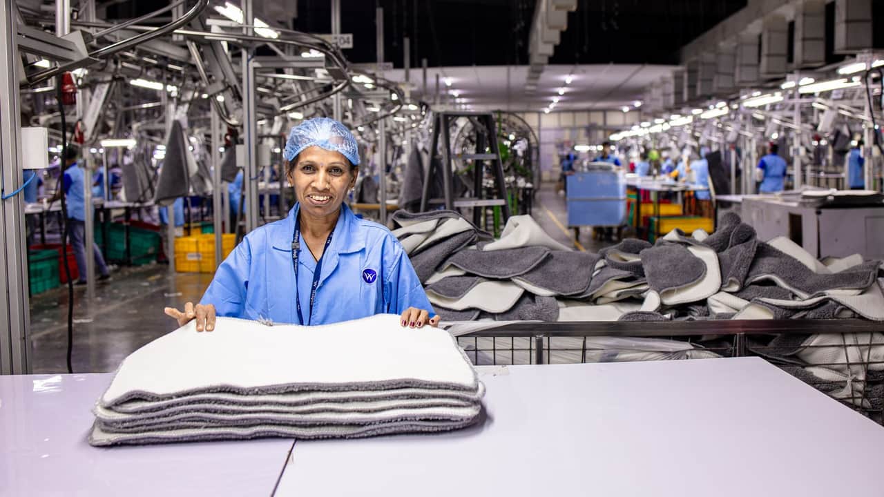 A textile worker in a factory folds products surrounded by industrial machines.