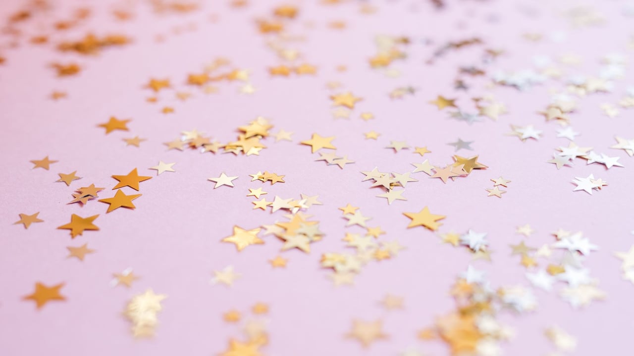 Scattered gold star confetti on a soft pink background for festive celebrations.