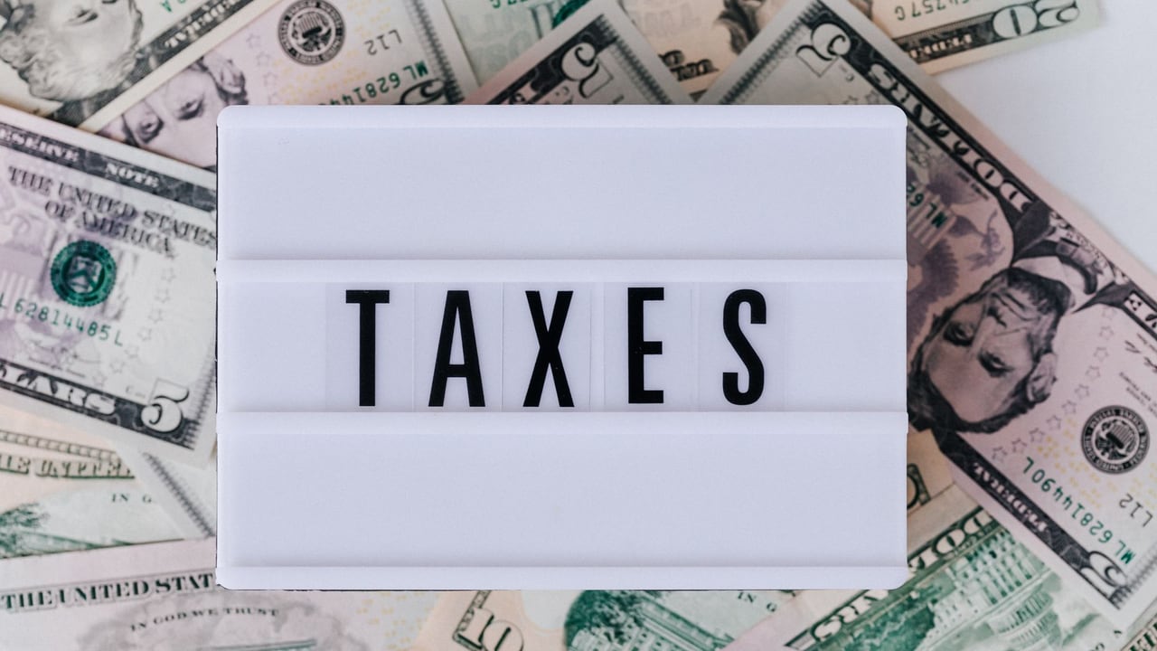 Top view of white vintage light box with TAXES inscription placed on stack of USA dollar bills on white surface