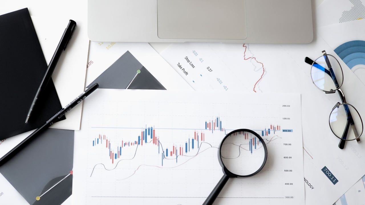 Flat lay of stock market analysis documents with magnifying glass, pens, and glasses.