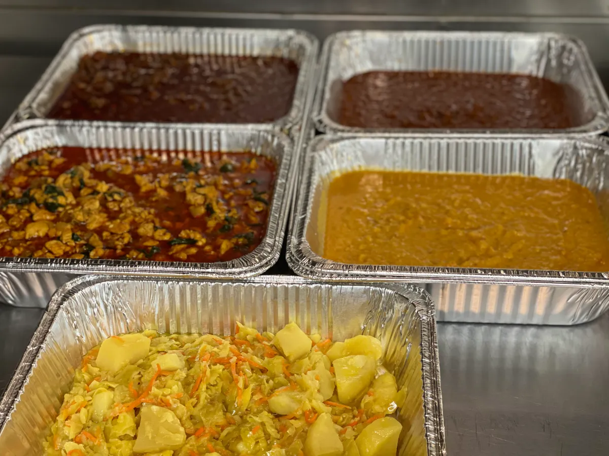A vibrant spread of rich, flavorful sauces in aluminum trays, paired with colorful cabbage and potato salad.