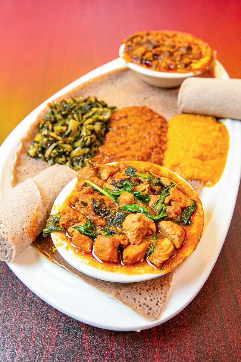 Satisfying Ethiopian platter featuring spicy chicken stew, lentils, sautéed greens, and injera on a vibrant backdrop.