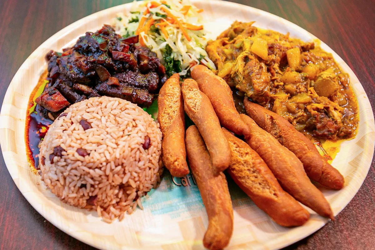 Savory rice and beans, spiced chicken stew, crispy plantains, and fresh coleslaw on a vibrant plate.