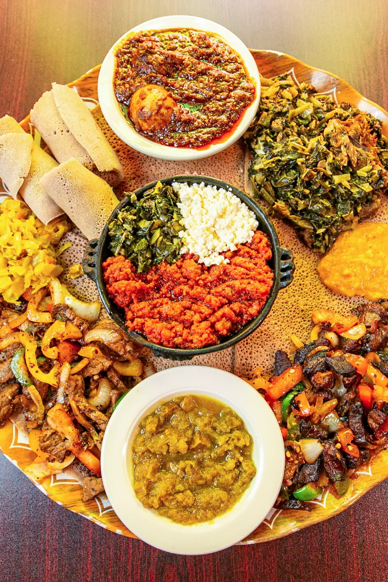 Vibrant platter of Ethiopian dishes featuring injera, spicy stews, sautéed vegetables, and fresh greens.
