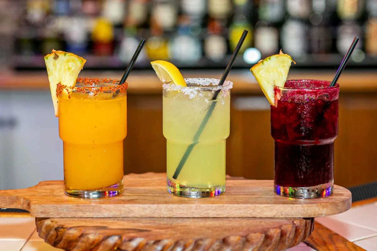 Vibrant cocktails featuring fruity flavors and garnishes, served on a rustic wooden board amidst a lively bar backdrop.