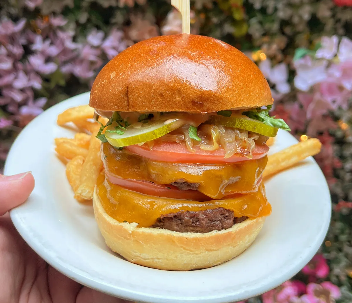 Delicious cheeseburger with melted cheddar, fresh tomato, pickles, and onions on a soft bun, served with crispy fries at Loreley Beer Garden in New York City. Perfect spot for birthdays, weddings, and corporate events in the Lower East Side, close to Nolita, Bowery,
