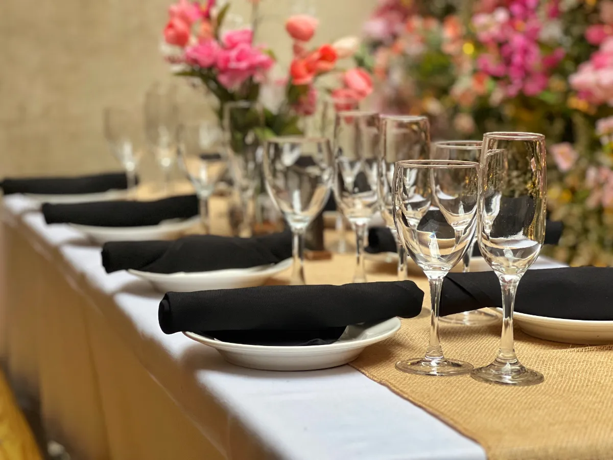 Elegant table setting with black napkins, wine glasses, and vibrant pink floral centerpiece, perfect for upscale dining experiences. Ideal for weddings, celebrations, and special events.