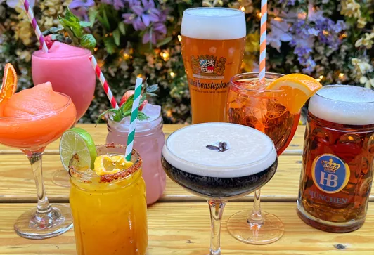 A vibrant assortment of colorful cocktails and beers at Loreley Beer Garden in NYCs Lower East Side, featuring the Strawberry Frozen Margarita, Purple Haze, and Weihenstephan Lager under a backdrop of lush greenery. Perfect for those searching for the best bar experience in the Lower East Side, with easy