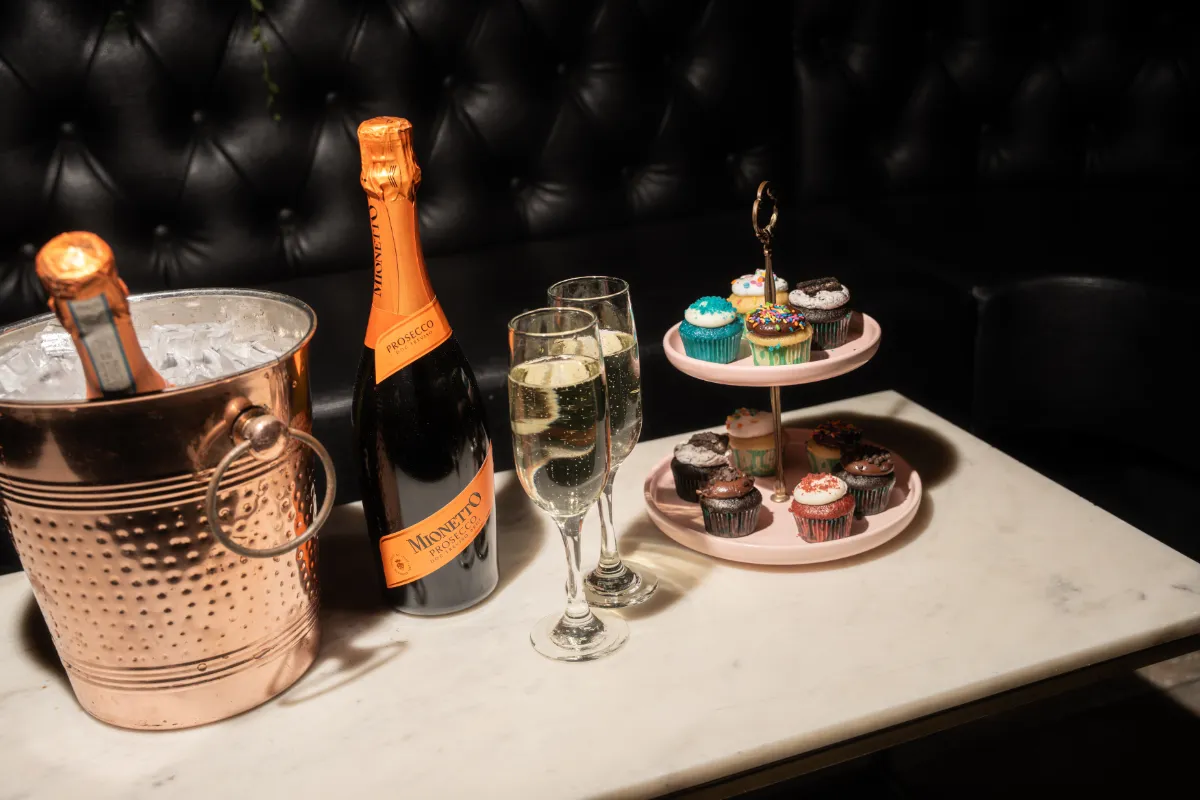 Charming setup featuring a bottle of Mionetto Prosecco in an ice bucket, two elegant glasses of sparkling wine, and a tiered dessert stand filled with colorful cupcakes at Loreley Beer Garden, an ideal spot for celebrations in NYCs Lower East Side neighborhood.