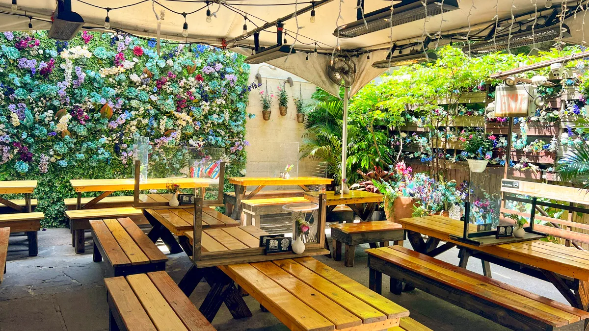 Outdoor seating area at Loreley Beer Garden featuring wooden tables, lush greenery, and vibrant flower wall decor, perfect for gatherings and events in NYCs Lower East Side neighborhood.