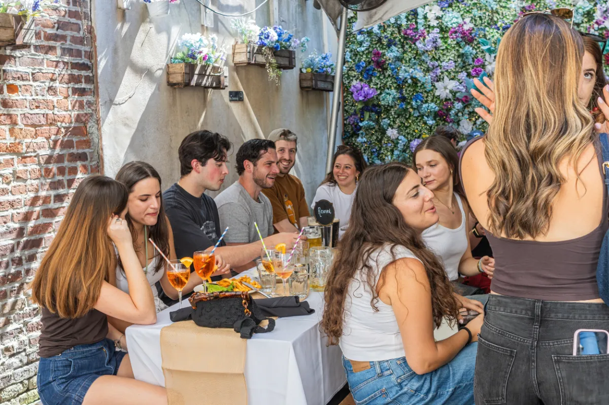 Group of friends enjoying vibrant cocktails and hearty plates at Loreley Beer Garden, a popular restaurant and bar in Manhattans Lower East Side, NY 10002. Perfect setting for birthdays, engagement parties, and more in a charming outdoor space adorned with flowers.