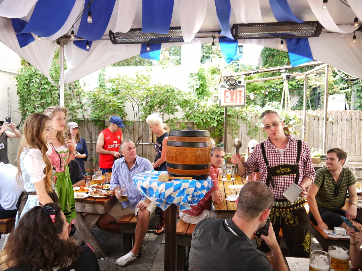 Guests enjoying a lively atmosphere at Loreley Beer Garden in NYCs Lower East Side, 10002. The image captures people dressed in traditional attire celebrating with beer and German dishes, highlighting the vibrant ambiance perfect for events like birthdays and engagement parties. Discover the best menu items, including pretzels
