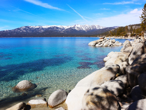 a rocky shore with clear blue water and mountains in the background