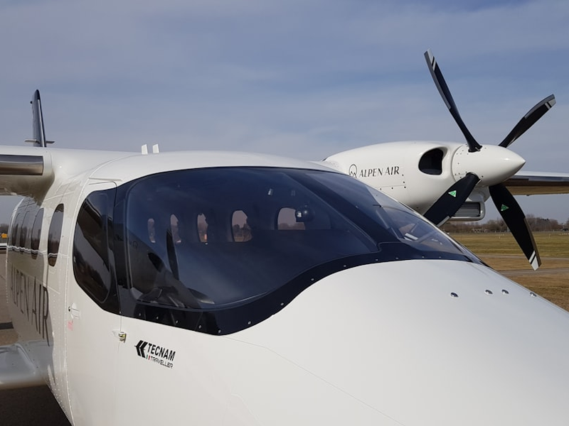 The front of the Alpen Air´s Tecnam P2012 Traveller aircraft on a field.