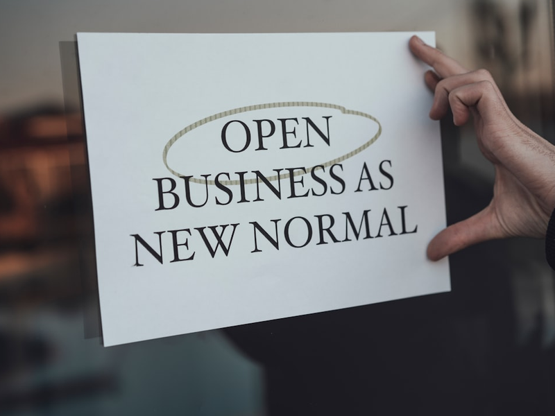 a person holding a sign that says open business as new normal