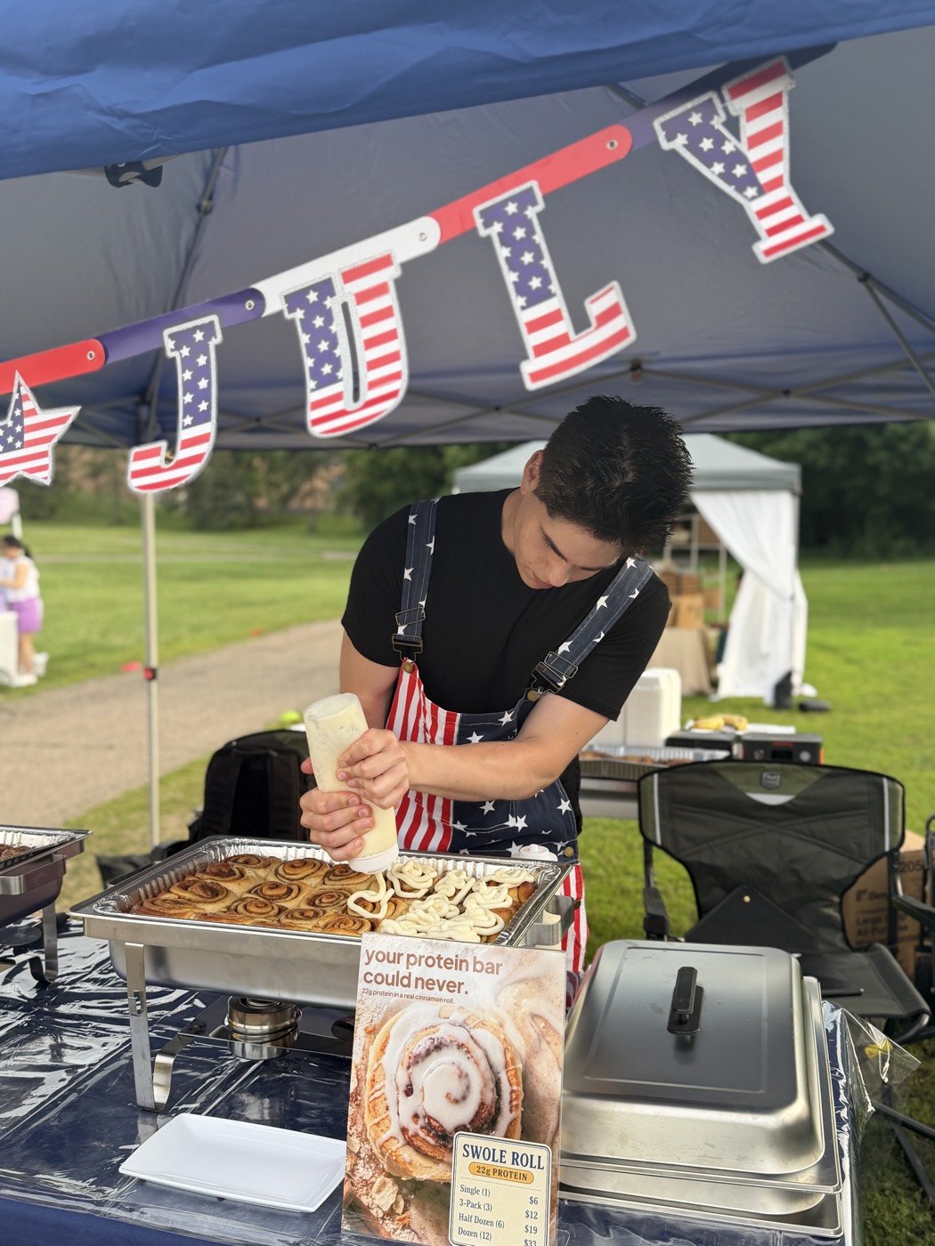 tommy frosting a tray of swole rolls in american-flag overalls at the tandoco farmers market booth