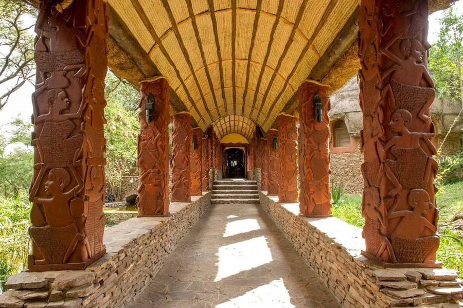 Covered walkway at Serengeti Serena Safari Lodge with carved African-style pillars leading toward the lodge entrance in Tanzania.