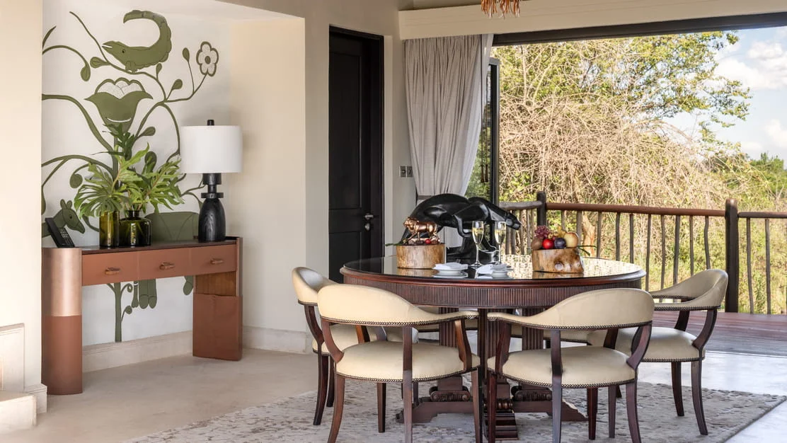 Luxury suite dining room with a round wooden table, plush chairs, and large glass patio doors in Serengeti.
