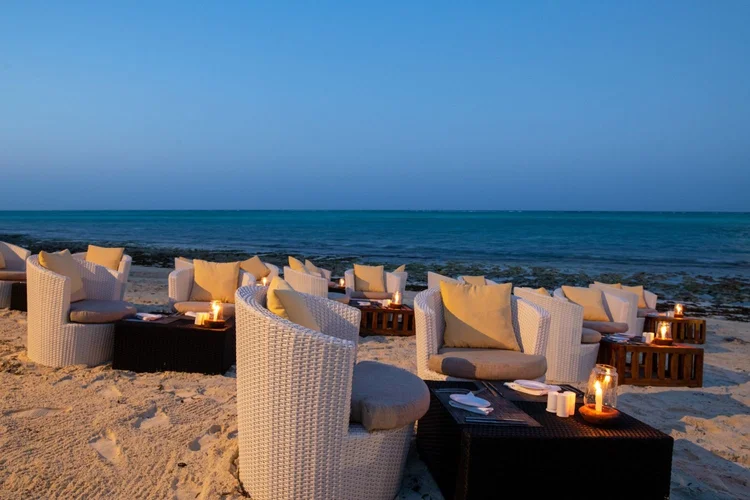 Cozy outdoor lounge seating area lit by candlelight near the ocean at dusk.