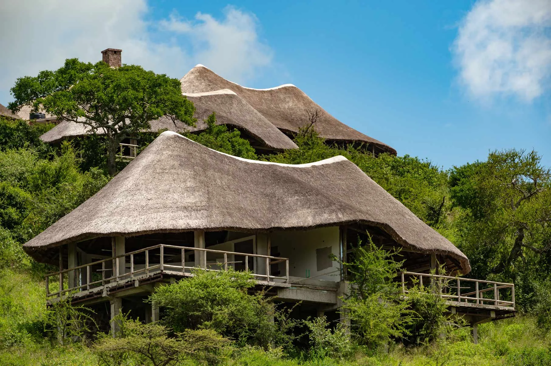 Thatched-roof luxury safari lodge nestled into lush green hills overlooking Serengeti Lake Magadi, Tanzania nature.