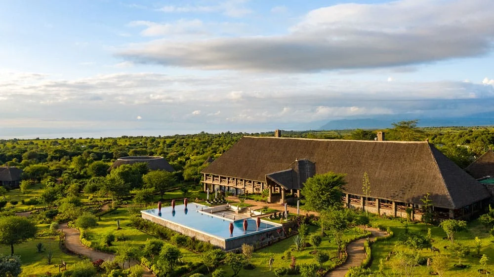 Panoramic view of the main thatch-roofed lodge, sprawling green gardens, and infinity pool.