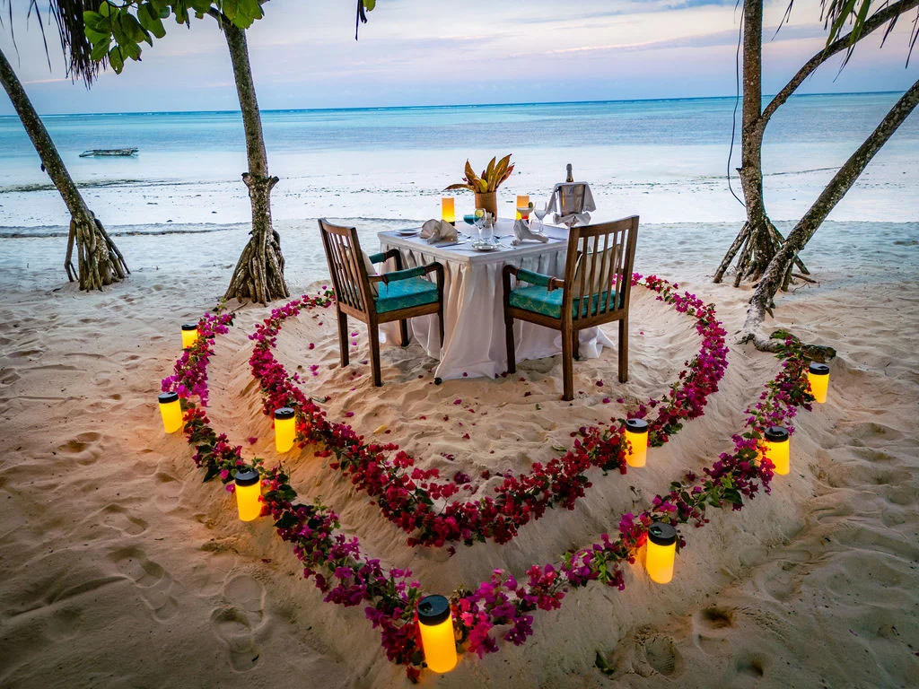 Romantic private beach dining setup surrounded by a heart-shaped flower display.