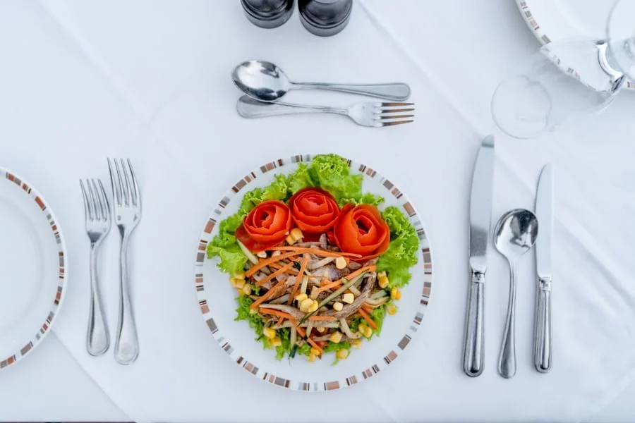 Overhead view of a gourmet fresh garden salad served with fine silver cutlery on a white tablecloth.