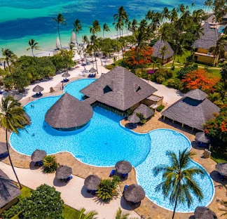 Aerial view of the large swimming pools, palm trees, and coastal beach at Neptune Pwani Beach Resort.