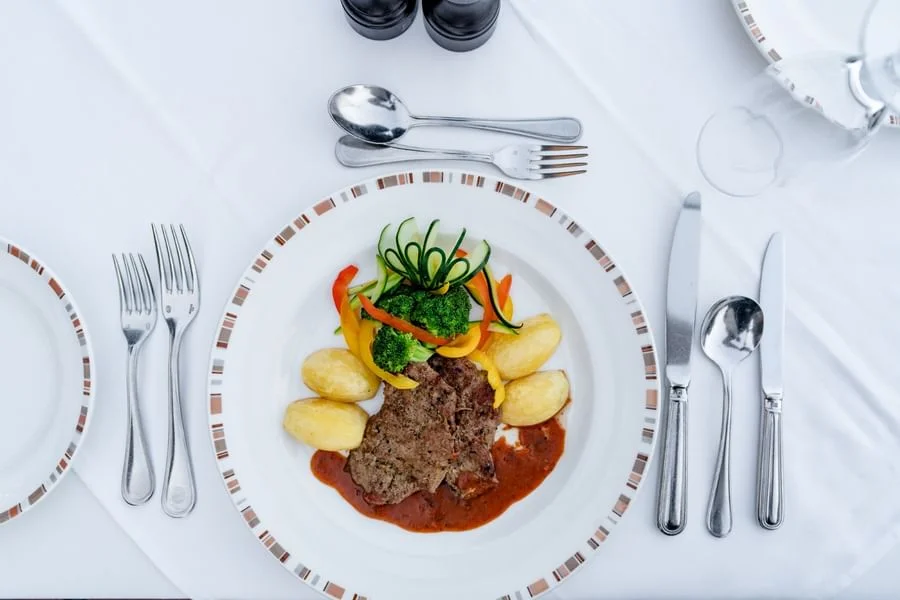Overhead view of a gourmet steak entree plated with potato rosti and silver cutlery on a white plate.