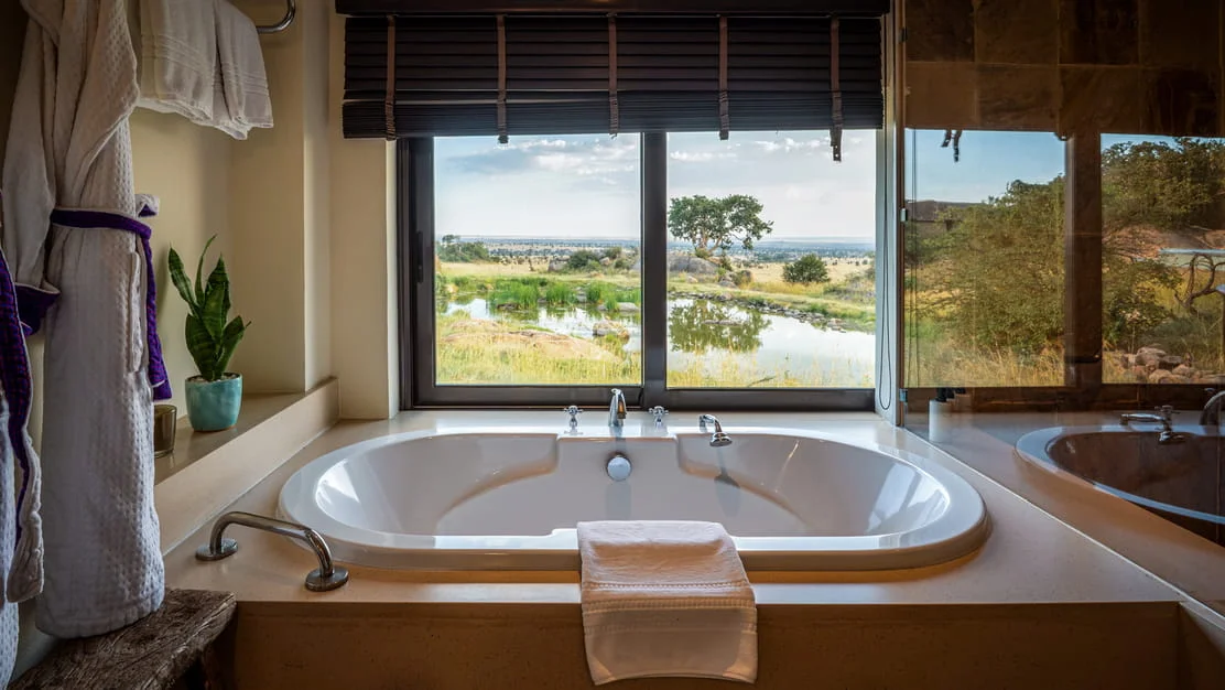 Deep ceramic soaking bathtub positioned in front of a large window overlooking the Serengeti landscape.