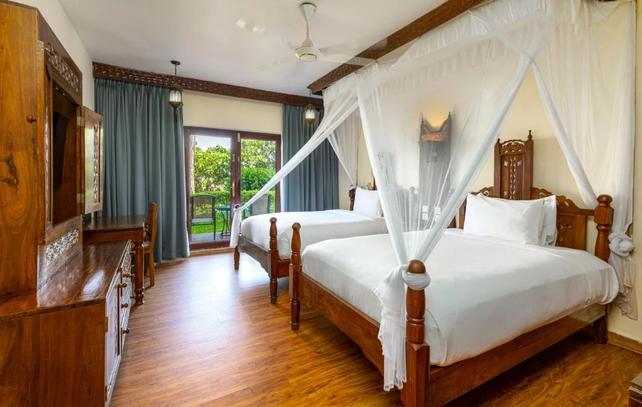 Elegant hotel bedroom suite featuring two canopy beds with mosquito nets.