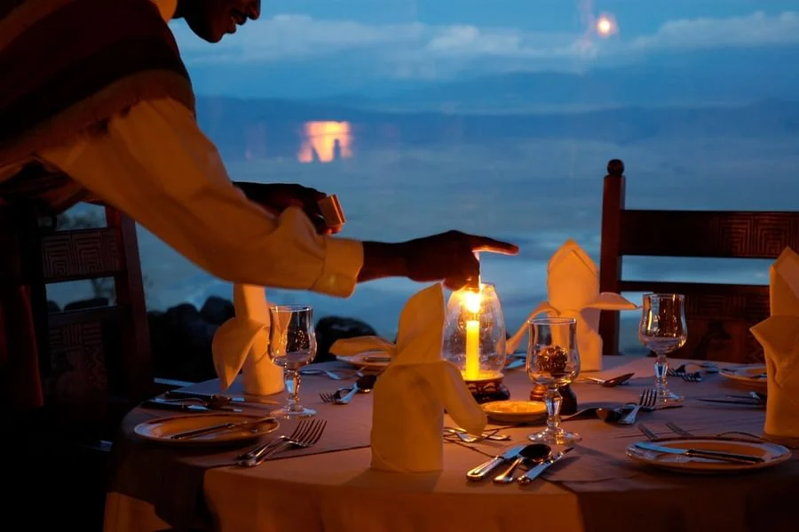 Candlelit dinner table with wine glasses set against a scenic mountain sunset backdrop in Ngorongoro.