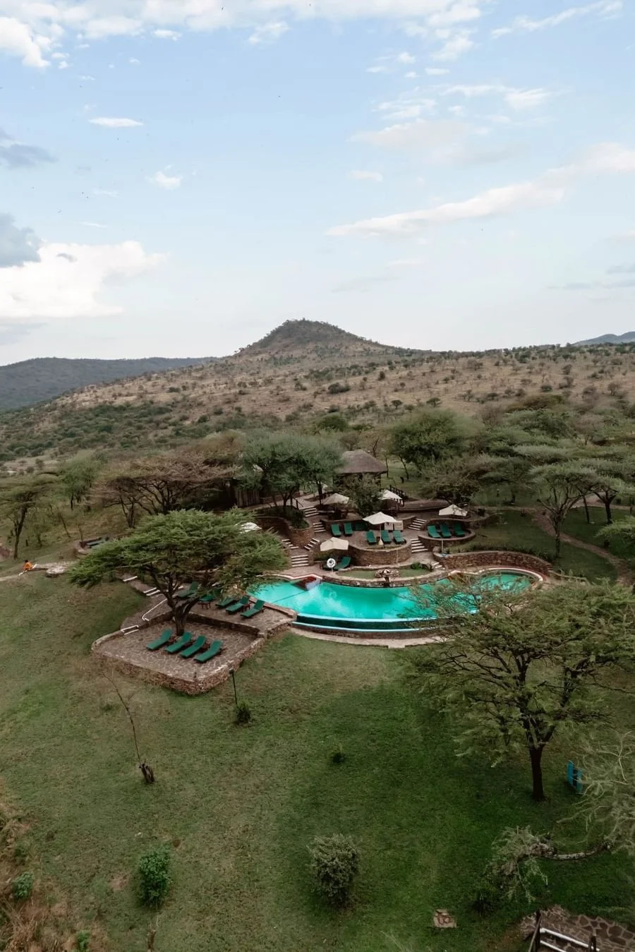 Aerial view of Serengeti Serena Safari Lodge swimming pool surrounded by trees, lawns and rolling hills in the Serengeti.