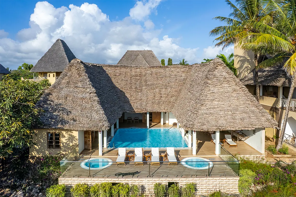 Traditional thatched-roof resort buildings surrounding a sparkling pool in Zanzibar.