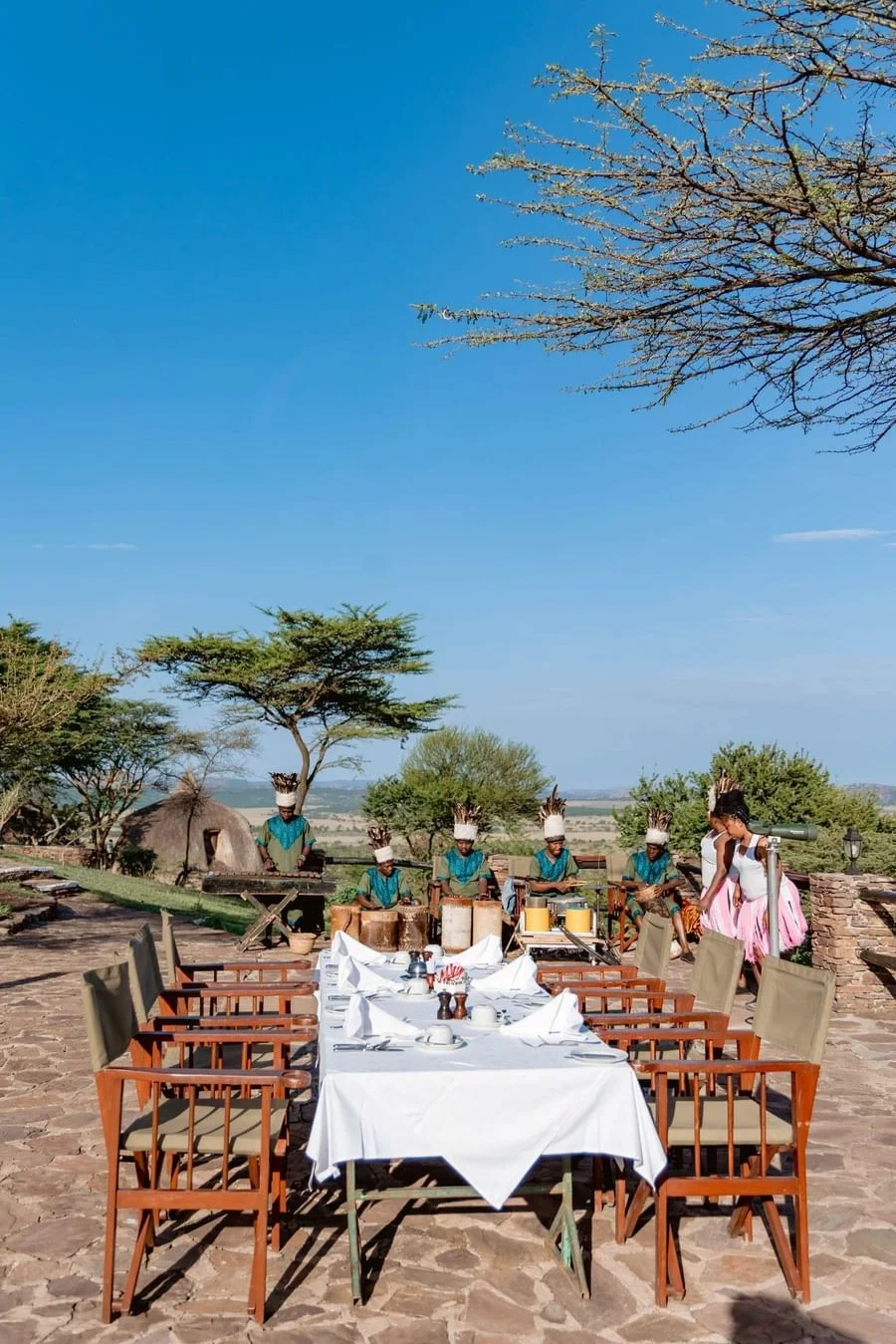 Outdoor dining setup at Serengeti Serena Safari Lodge with white tablecloths, wooden chairs and open savannah views.