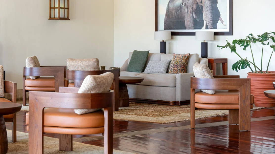 Deluxe suite seating nook with wooden armchairs, glass coffee table, and tropical plants in Serengeti.